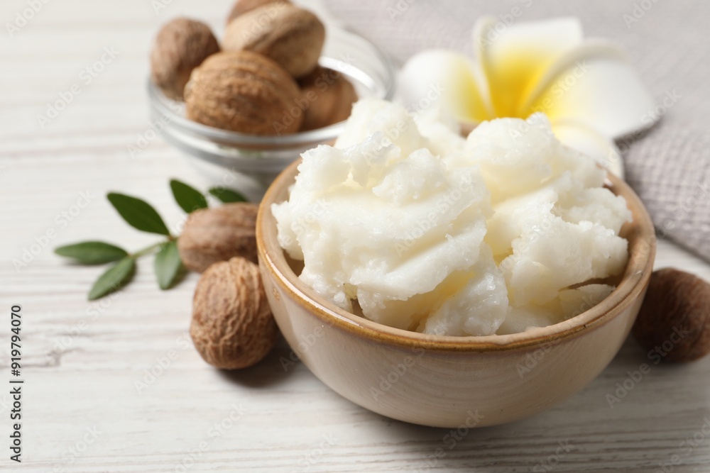 Shea butter in bowl, flower and nuts on white wooden table, closeup Shea butter in bowl, flower and nuts on white wooden table, closeup