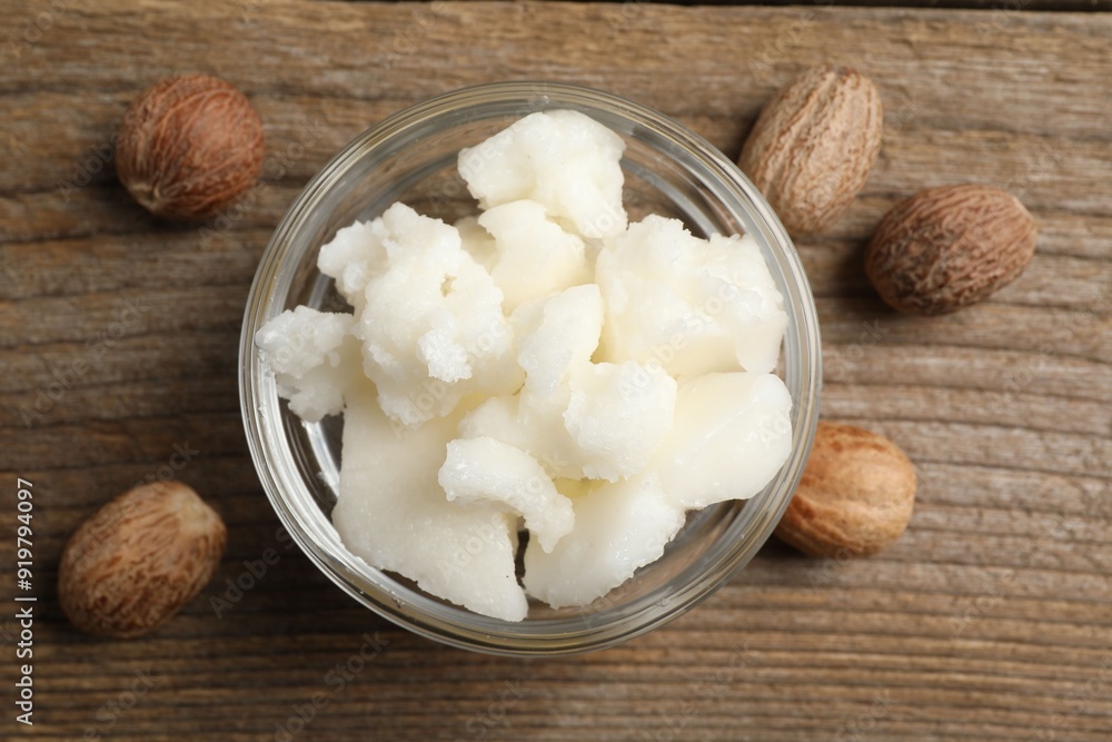 Shea butter in bowl and nuts on wooden table, flat lay Shea butter in bowl and nuts on wooden table, flat lay