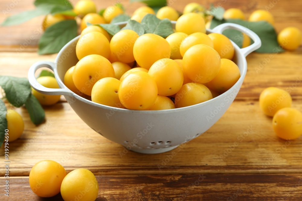 Tasty ripe plums and leaves in colander on wooden table, closeup Tasty ripe plums and leaves in colander on wooden table, closeup