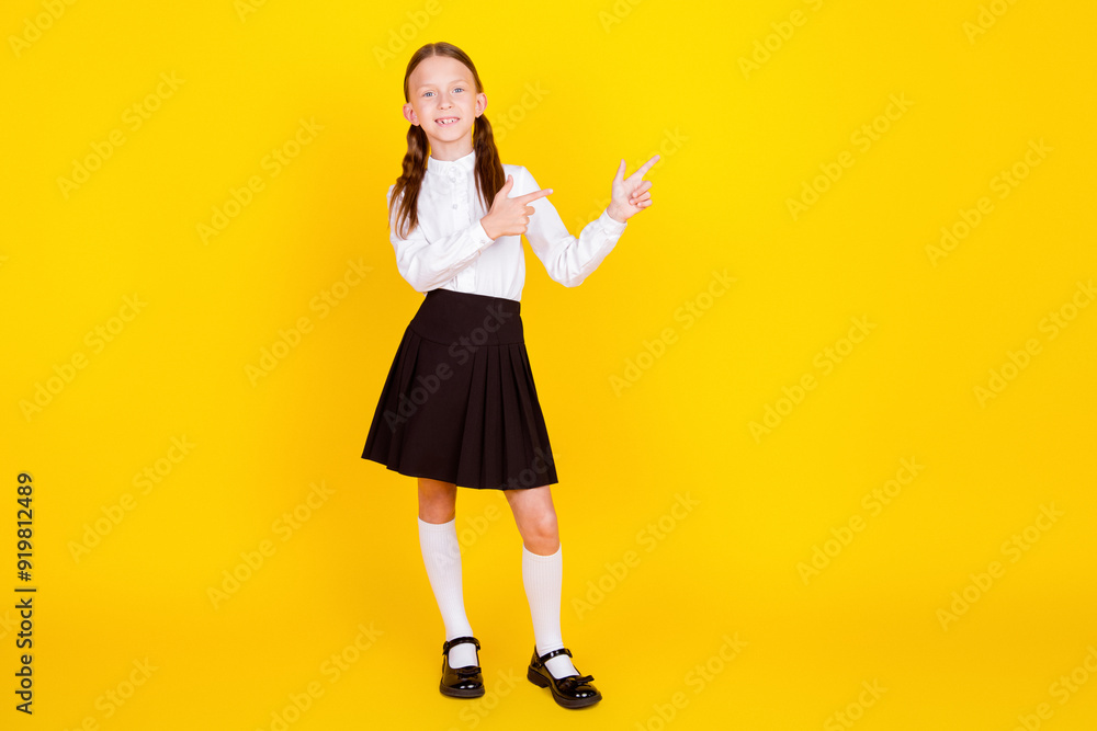 Full length photo of lovely small schoolgirl point empty space dressed stylish uniform isolated on yellow color background Full length photo of lovely small schoolgirl point empty space dressed stylish uniform isolated on yellow color background