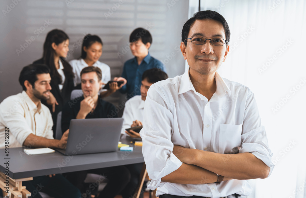 Confidence and happy smiling businessman portrait with background of his colleague and business team working in office. Office worker teamwork and positive workplace concept. Prudent Confidence and happy smiling businessman portrait with background of his colleague and business team working in office. Office worker teamwork and positive workplace concept. Prudent