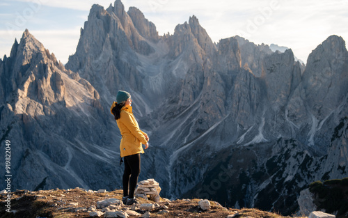 A woman hikes in the mountains, her attire suitable for the crisp atmosphere, as she observes the rugged terrain that surrounds her, reflecting a sense of adventure and discovery. photo