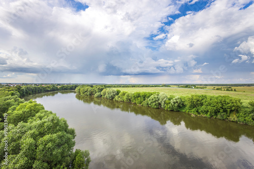 A picturesque river meanders through vibrant greenery under a striking sky filled with dynamic clouds at dusk. photo