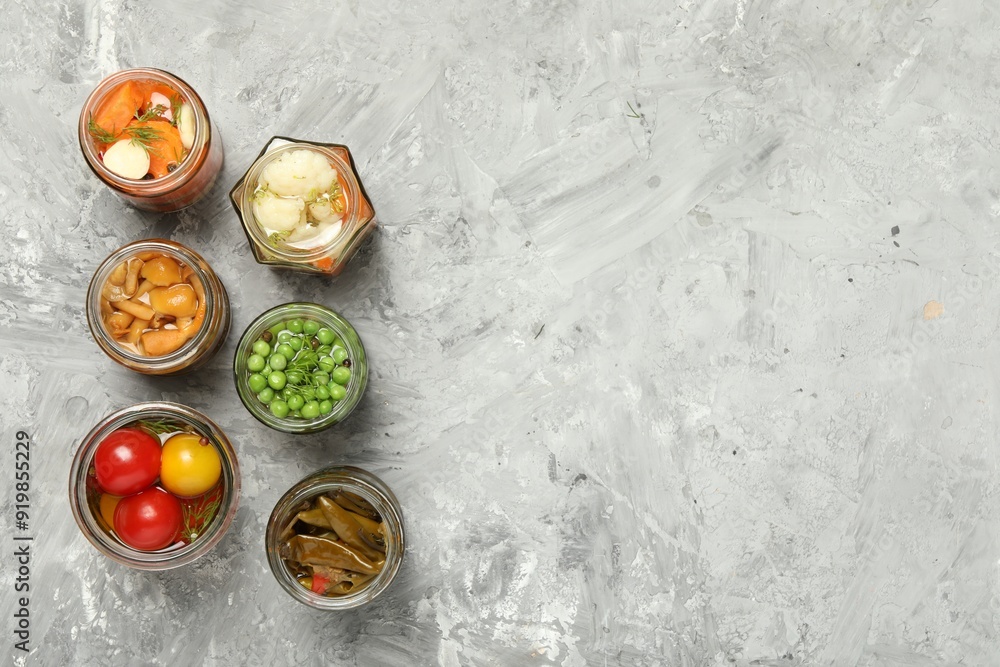 Different pickled products in jars on grey table, flat lay. Space for text