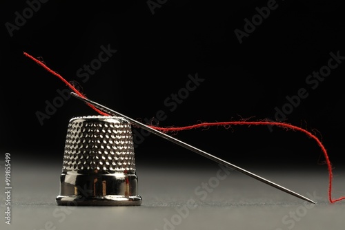 Bilde på lerret Sewing needle with red thread and thimble on grey table against black background