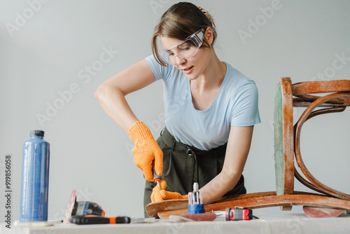 Woman restoring old furniture using screwdriver in workshop