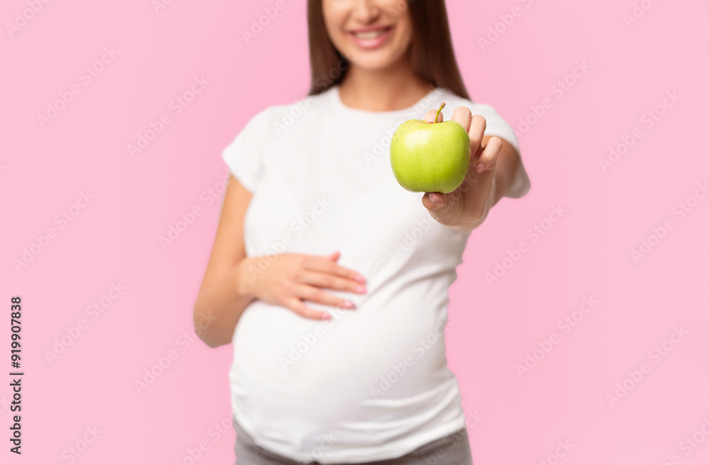 Unrecognizable Pregnant Girl Offering Green Apple To Camera Standing Touching Belly Over White Studio Background. Cropped Unrecognizable Pregnant Girl Offering Green Apple To Camera Standing Touching Belly Over White Studio Background. Cropped