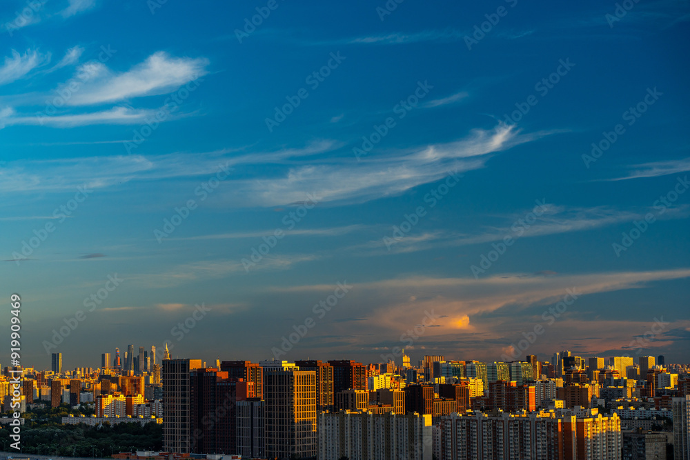 Fototapeta premium A beautiful sunset over a big city, high-rise residential buildings and skyscrapers illuminated by the setting sun against the blue sky. View from above. Moscow, Khovrino district.