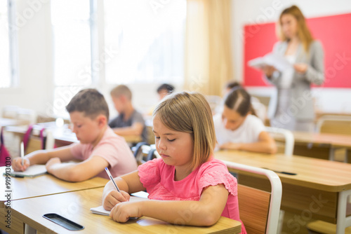 Photos Portrait of cute intelligent schoolgirl who writing exercises at lesson in prima