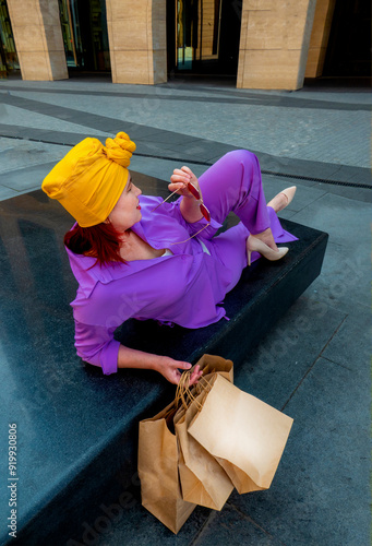 Obraz na płótnie woman with craft shopping bags in the city. The concept of fashionable Consumerism and ecology. Adult Asian woman in a purple suit with red and yellow accents enjoys shopping. rest between purchases w salonie