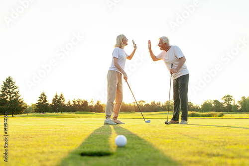 An elderly couple in sportswear exchange greetings on a golf course after a successful shot. Man and woman playing and succeeding together. Sunny day in the background 