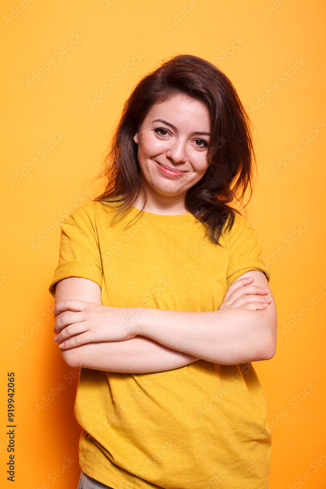 Smiling woman standing in front of camera, arms crossed, radiating confidence. Portrait of caucasian lady standing in a studio against isolated orange background, grinning and posing. Smiling woman standing in front of camera, arms crossed, radiating confidence. Portrait of caucasian lady standing in a studio against isolated orange background, grinning and posing.