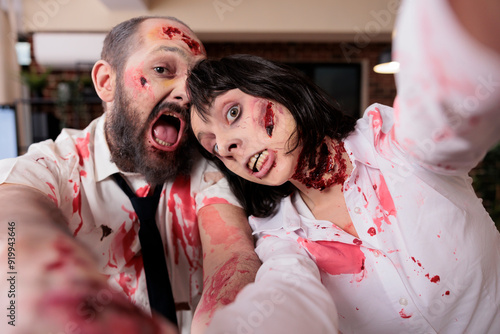 Actors having fun in office horror movie set dressed as zombies taking selfies doing comical expressions. Man and woman playing in thriller film shooting behind the scenes footage, goofing around, POV