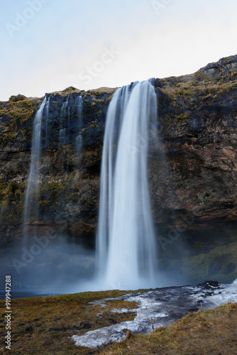 River stream from icelandic cascade flowing down off cliff, water flow falling off snowy frozen mountain or hill. Breathtaking natural seljalandsfoss waterfall in iceland, wild polar landscape.