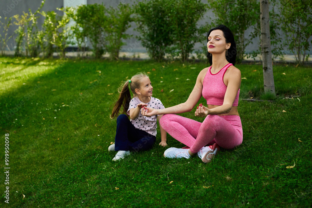 Fototapeta premium Mother and daughter practicing meditation on green grass in a peaceful outdoor setting