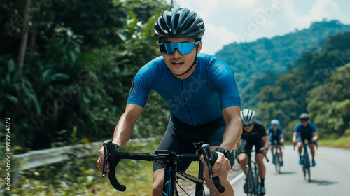 A group of cyclists, led by an Asian man in a blue jersey, cycling on a road surrounded by greenery.