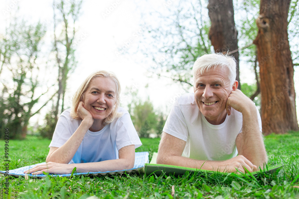 elderly athletic couple seniors man and woman lying on yoga mat and relaxing in park outdoors, gray-haired grandparents doing yoga and meditating and smiling in nature elderly athletic couple seniors man and woman lying on yoga mat and relaxing in park outdoors, gray-haired grandparents doing yoga and meditating and smiling in nature