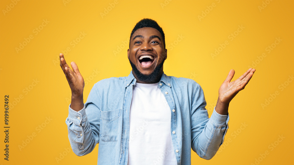 © Prostock-studio - I can not believe. Portrait of joyful african american man raising hands in the air with excitement and looking at camera, yellow studio background.