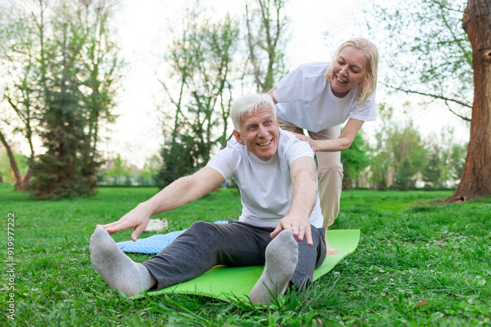 Fototapeta premium elderly senior couple man and woman doing yoga and meditating in a park in open space, gray-haired grandparents doing sports and active lifestyle in nature