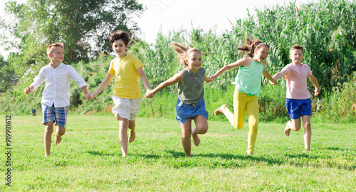 Group of cheerful tweens running together in city park on sunny summer day. Happy healthy childhood concept..