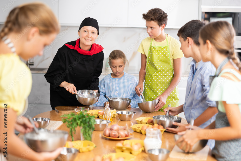 © JackF - Smiling woman, qualified chef wearing black cook jacket and cap, conducting culinary masterclass for teenage children, sharing secrets of cooking © JackF - Smiling woman, qualified chef wearing black cook jacket and cap, conducting culinary masterclass for teenage children, sharing secrets of cooking