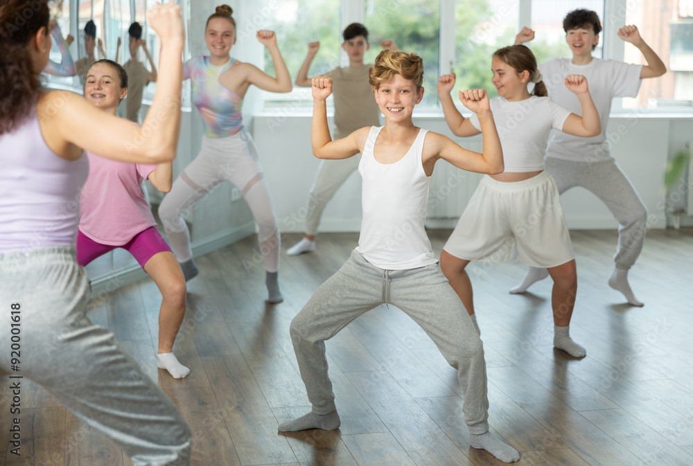 Fototapeta premium Guy teen performs modern dances repeats movements of unrecognizable teacher together with friends during lesson at choreographic school. Hobbies, active pastime