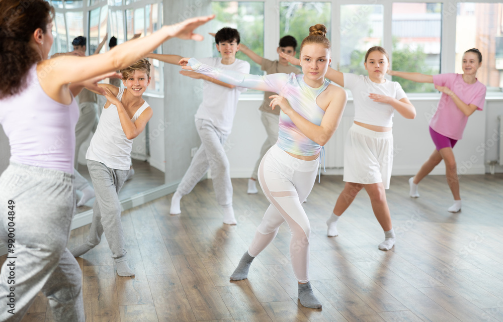 Fototapeta premium Young girls and boys repeat the movements of dance teacher, training in a spacious studio