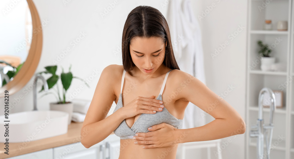 Young woman checking her breast in bathroom. Cancer awareness concept Young woman checking her breast in bathroom. Cancer awareness concept