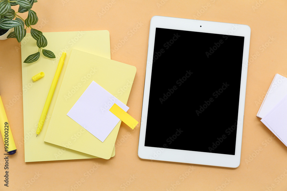 Tablet with notebooks and sticky notes on orange background Tablet with notebooks and sticky notes on orange background