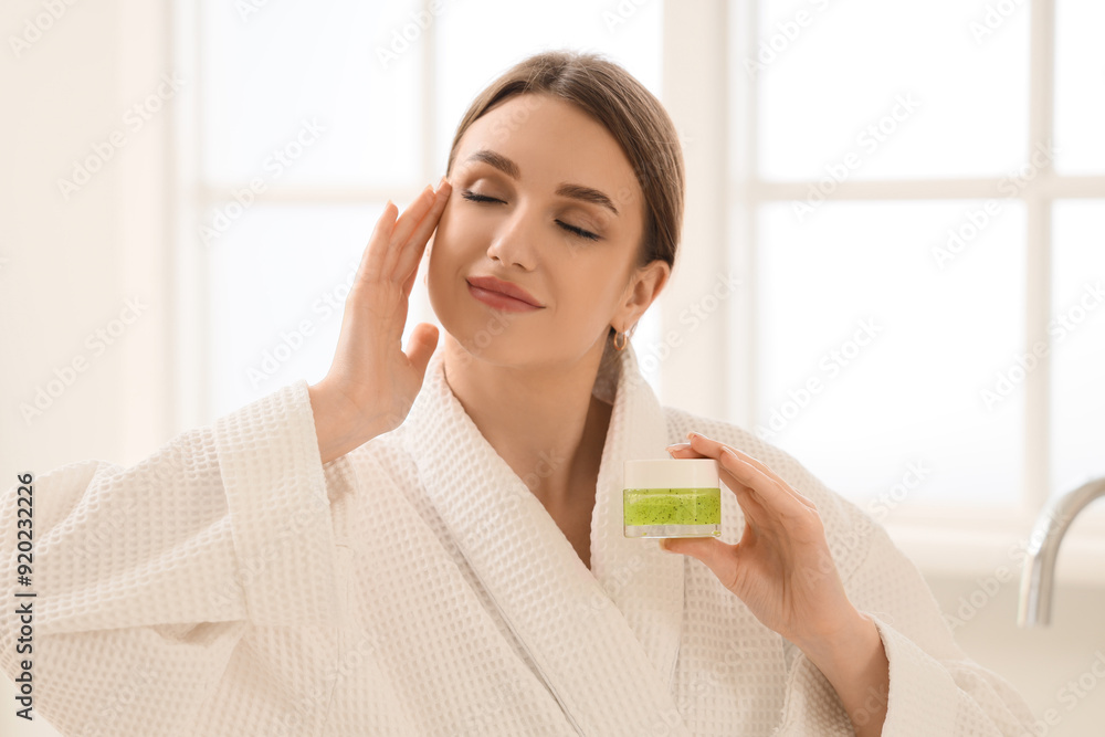 Beautiful young woman with jar of cosmetic cream near window at home Beautiful young woman with jar of cosmetic cream near window at home