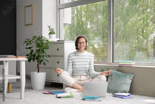 Beautiful student in headphones meditating on floor at home