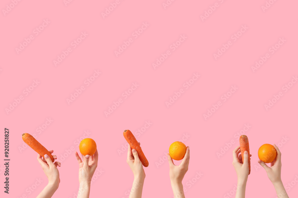 Hands with fresh oranges and carrots on pink background