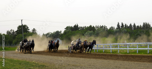Three chuckwagons kicking up dust as they race around in a track in a country fair in Saskatchewan