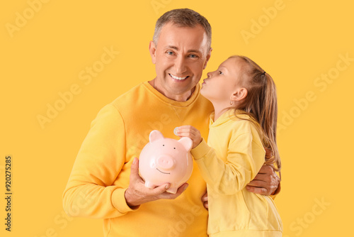 Little girl with her father holding piggy bank on yellow background