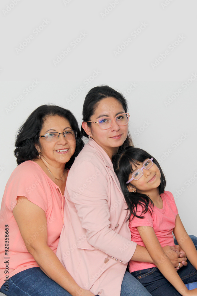 Three generations of brunette Latina women, grandmother, mom and daughter with glasses sitting together spending quality time and celebrating Mother's Day Three generations of brunette Latina women, grandmother, mom and daughter with glasses sitting together spending quality time and celebrating Mother's Day