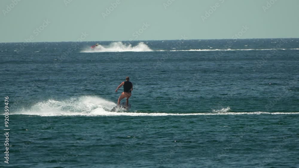 A motorized surfboard with a rider moving on a calm sea. The silhouette of a man on a water scooter glides through the water. Sports and sea activities on a beach holiday. Slow motion. A motorized surfboard with a rider moving on a calm sea. The silhouette of a man on a water scooter glides through the water. Sports and sea activities on a beach holiday. Slow motion.