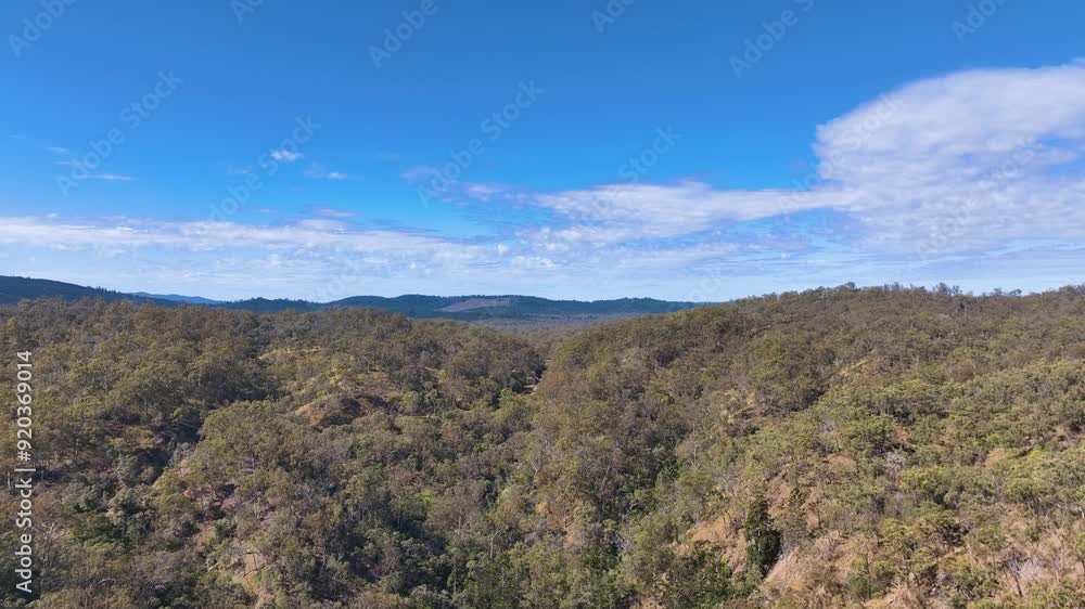 Aerial rises above the Barimoon area, and forest covered hills to expose the Boyd Burnett Rail Trail cutting through the woodlands with views to Kalpower State Forest Central Queensland Australia. Aerial rises above the Barimoon area, and forest covered hills to expose the Boyd Burnett Rail Trail cutting through the woodlands with views to Kalpower State Forest Central Queensland Australia.