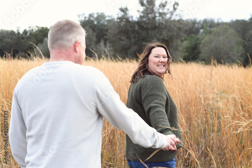 Smiling woman holding hands with a man, walking through a field photo