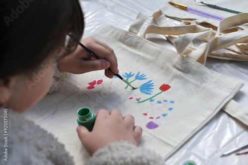 Child lefthander paints a canvas bag with acrylic paints. photo