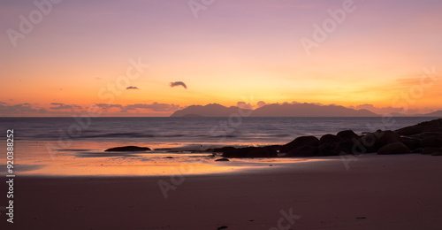 Glorious colors at sunrise with silhouetted rocks and reflections in the water on the beach at Rose Bay in Bowen a popular tourist destination in the Whitsunday region of Queensland, Australia.