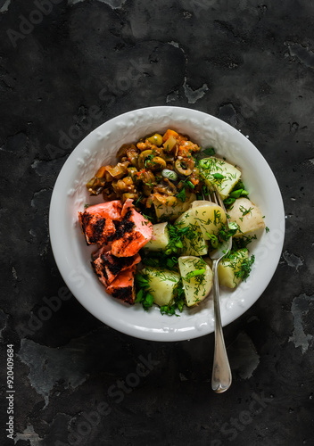 Simple outdoor food - boiled potatoes with herbs, grilled salmon, caponata on a dark background, top view photo