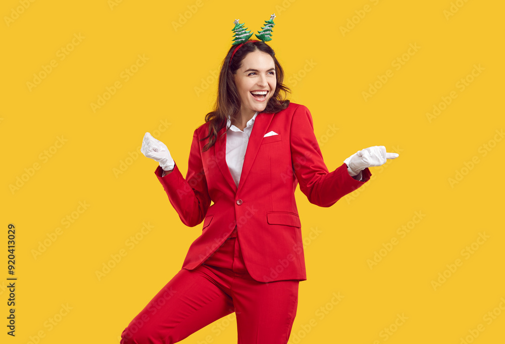 New Year's mood and fun. Beautiful stylish woman dancing having fun new year occasion on orange background in studio. Girl in red suit, white gloves and decorative New Year's hoop on head is smiling. New Year's mood and fun. Beautiful stylish woman dancing having fun new year occasion on orange background in studio. Girl in red suit, white gloves and decorative New Year's hoop on head is smiling.