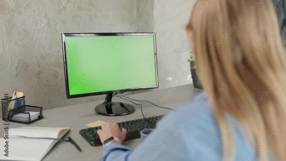 Young Woman Working In Office On Desktop Computer with Green Screen Mock Up Display. Girl Drinks Coffee And Looks At Green Chromakey Monitor Young Woman Working In Office On Desktop Computer with Green Screen Mock Up Display. Girl Drinks Coffee And Looks At Green Chromakey Monitor