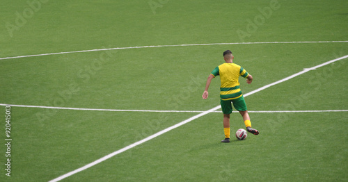 Football player in the midfield area preparing a passing movement with yellow and green equipment, synthetic green