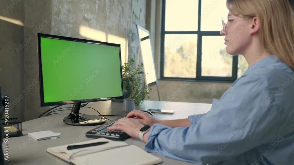 Young Woman Working In Office On Desktop Computer with Green Screen Mock Up Display. Girl Typing on Keyboard And Looks At Green Chromakey Monitor Young Woman Working In Office On Desktop Computer with Green Screen Mock Up Display. Girl Typing on Keyboard And Looks At Green Chromakey Monitor