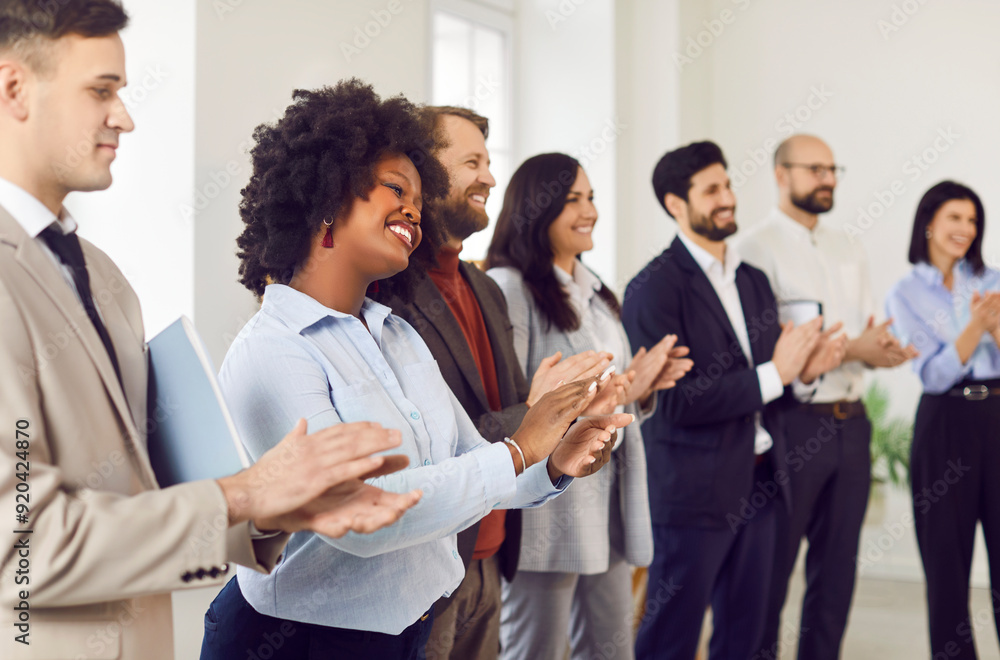 Group of smiling diverse business people men and women applauding to speaker standing in a row. Side view portrait of happy business team clapping after successful business training or conference. Group of smiling diverse business people men and women applauding to speaker standing in a row. Side view portrait of happy business team clapping after successful business training or conference.