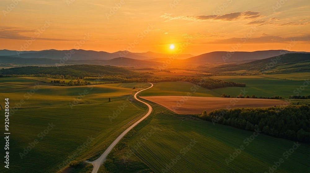 Aerial view of a winding dirt road through a rolling landscape, with a sun setting in the distance. Aerial view of a winding dirt road through a rolling landscape, with a sun setting in the distance.