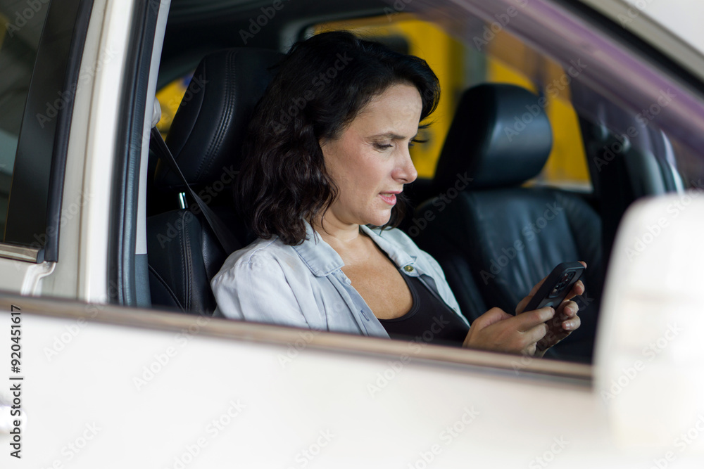 A woman is sitting in a car, looking at her phone, appearing to type or read something important on it. A woman is sitting in a car, looking at her phone, appearing to type or read something important on it.