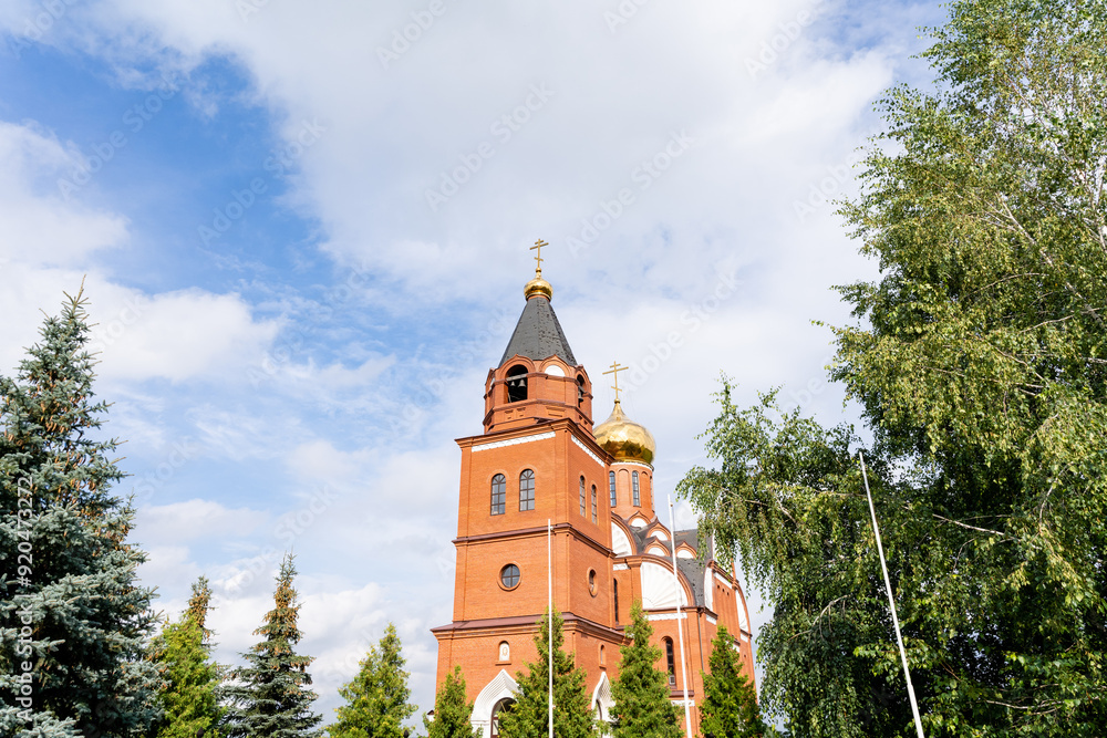 A large red brick church featuring an impressive bell tower is beautifully surrounded by lush green trees that enhance its stunning appearance and contribute to the serene atmosphere A large red brick church featuring an impressive bell tower is beautifully surrounded by lush green trees that enhance its stunning appearance and contribute to the serene atmosphere