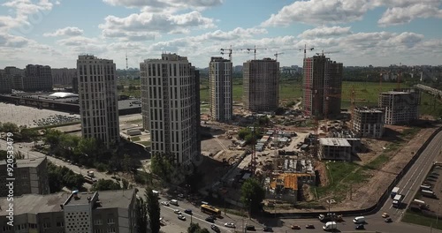 Aerial view of a construction site with high-rise buildings in progress. The urban landscape shows cranes, machinery, and incomplete structures set against a modern city skyline. Ideal for urbanizatio